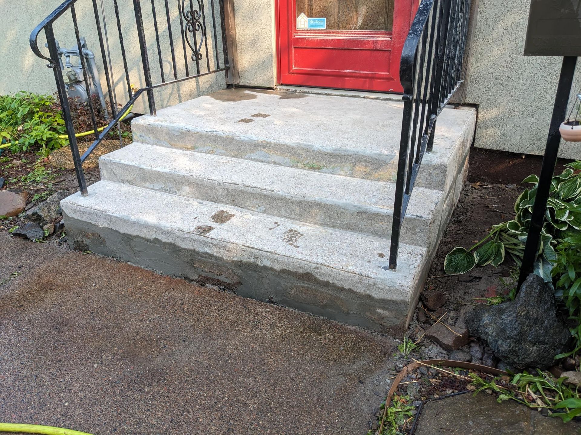A set of concrete steps leading up to a red door with a wrought iron railing.
