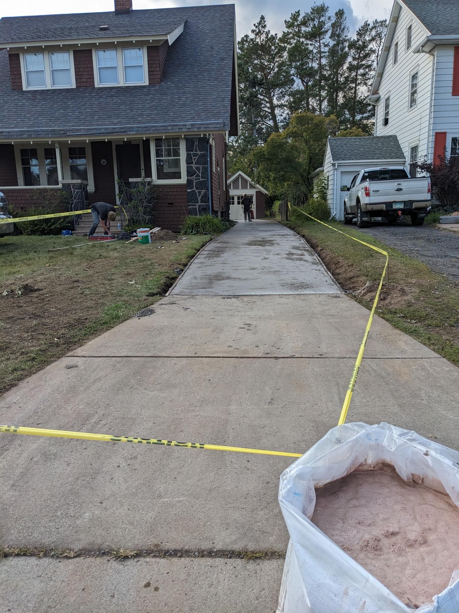 A bag of sand is sitting on the sidewalk in front of a house.