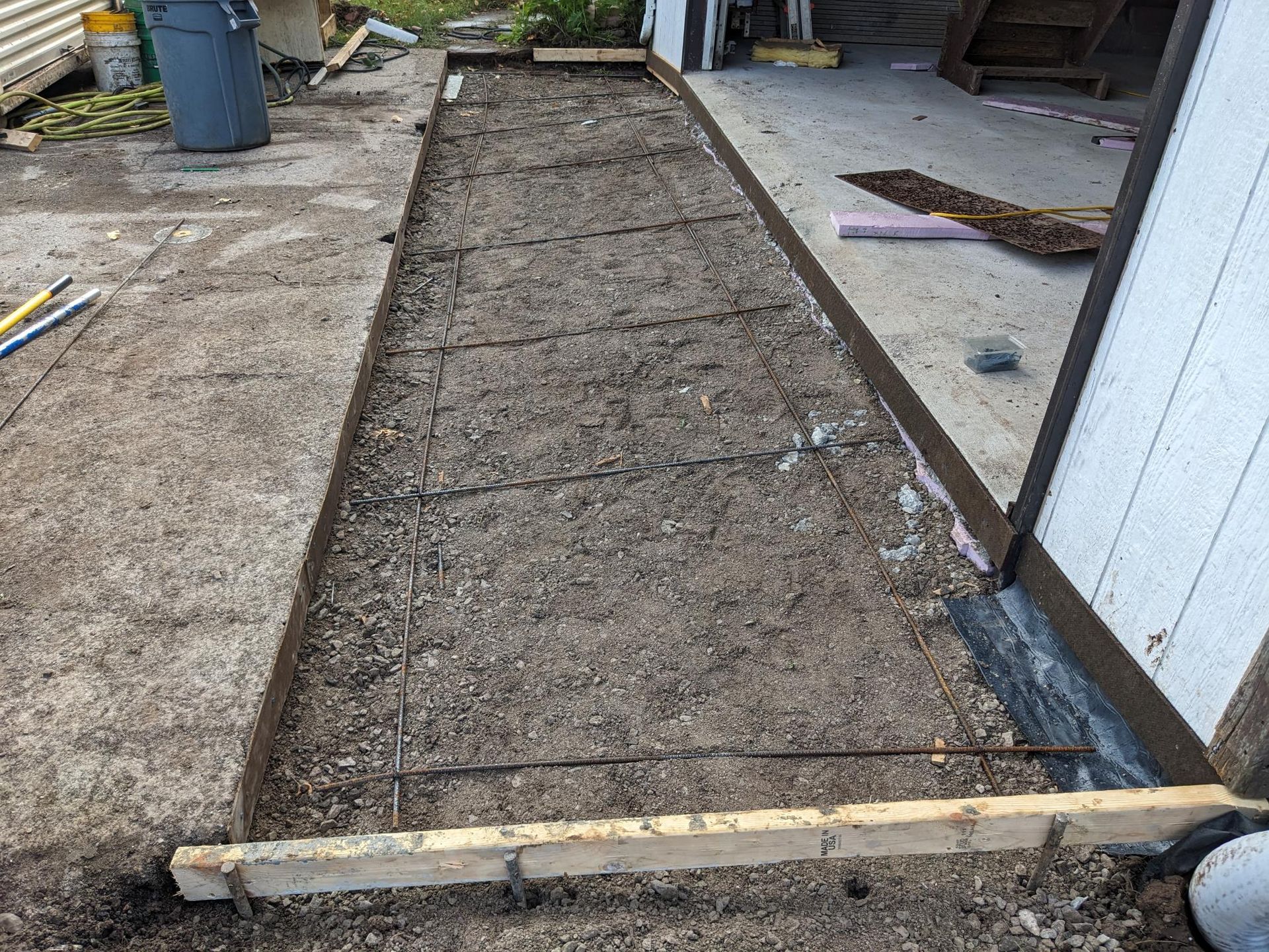 A concrete walkway is being built in front of a garage.
