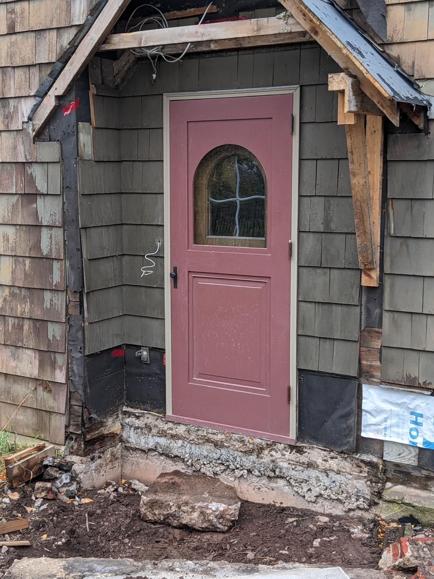 A pink door with a round window is on the side of a building.