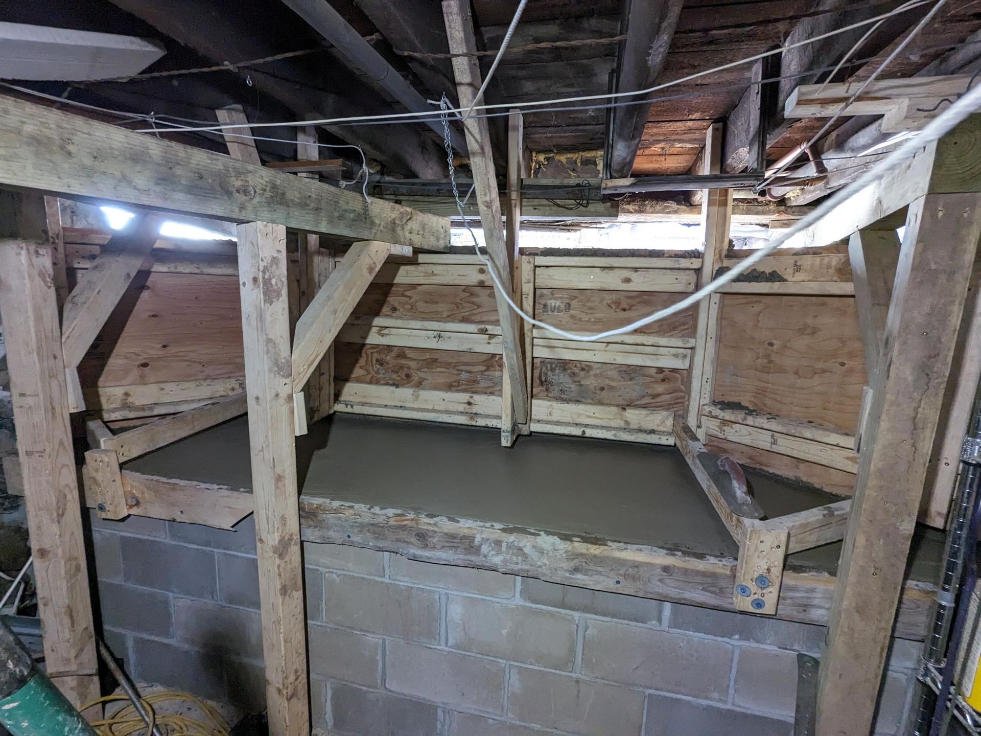 A concrete floor is being poured in a basement under a wooden structure.