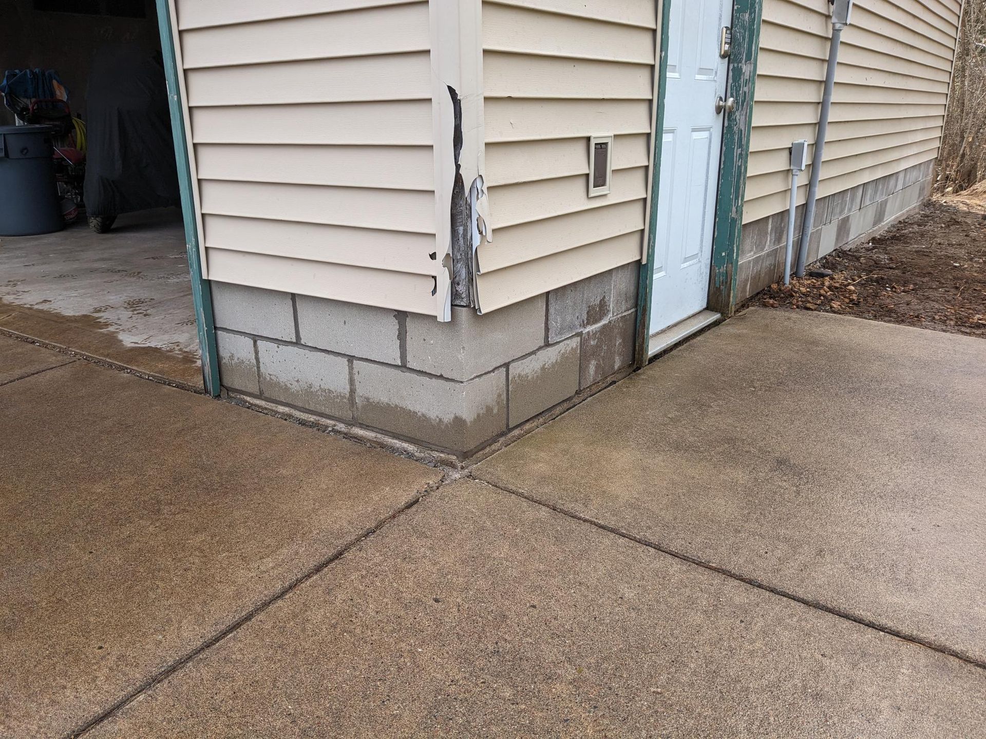 A corner of a house with a concrete sidewalk in front of it