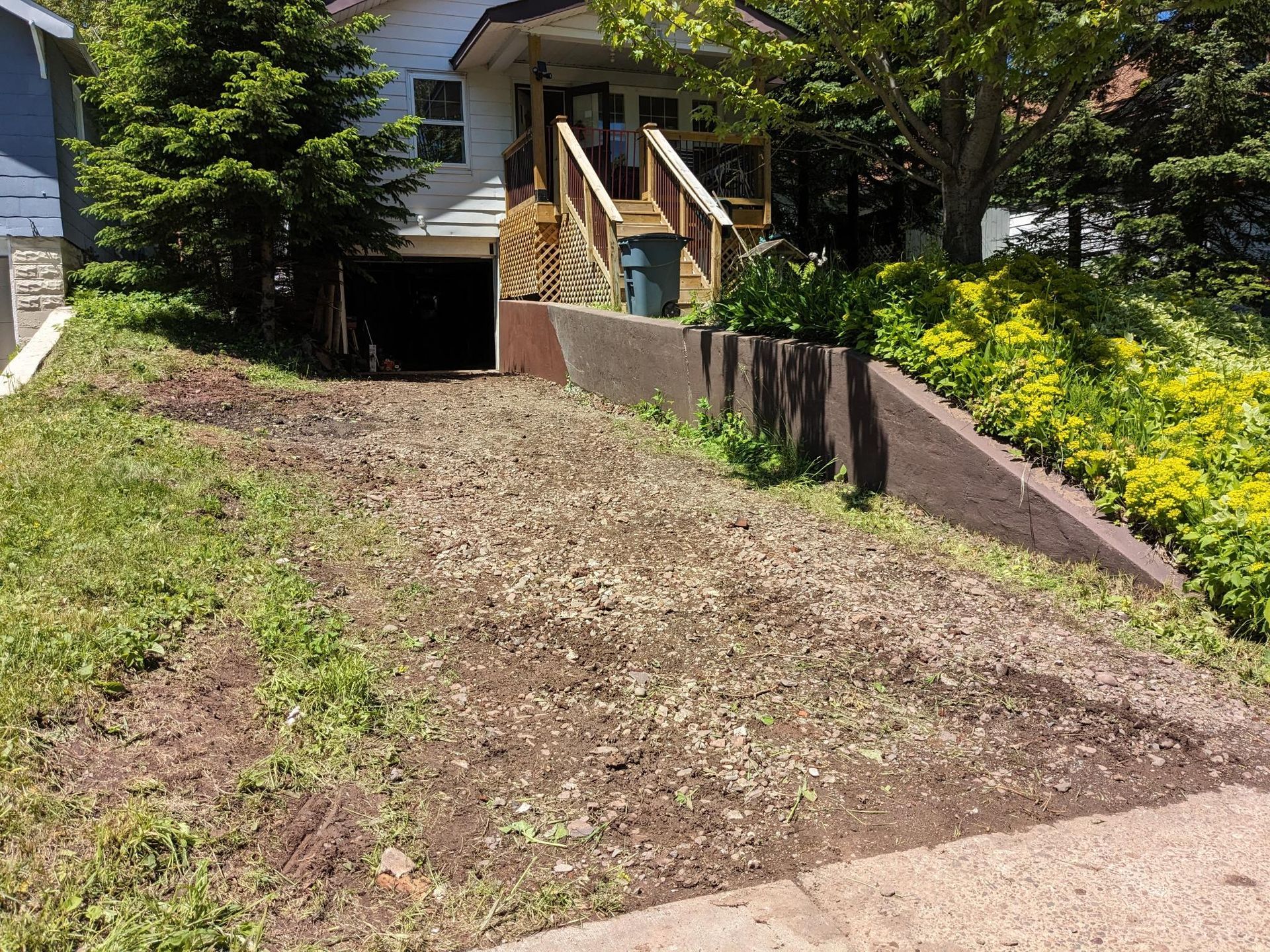 A dirt driveway leading to a house with a deck.