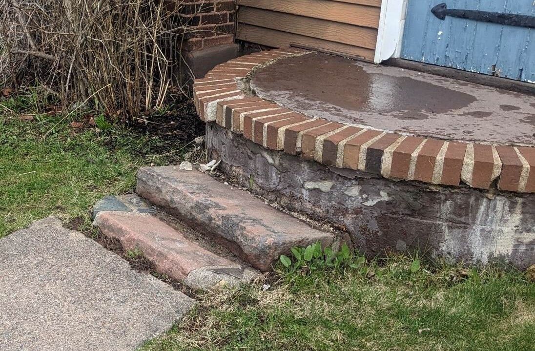 A brick porch with steps leading up to it and a blue door.