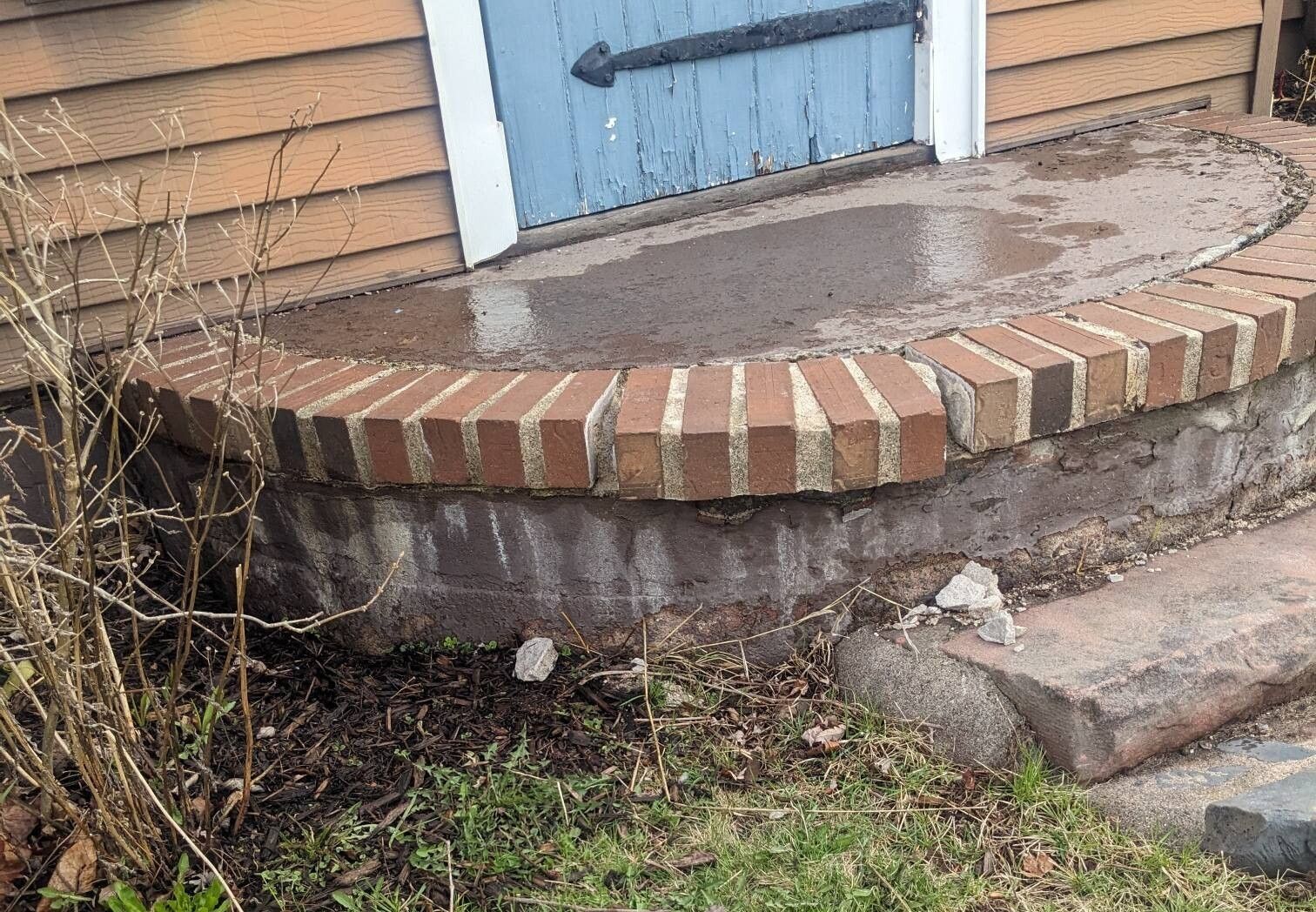 A brick porch with a blue door in the background.