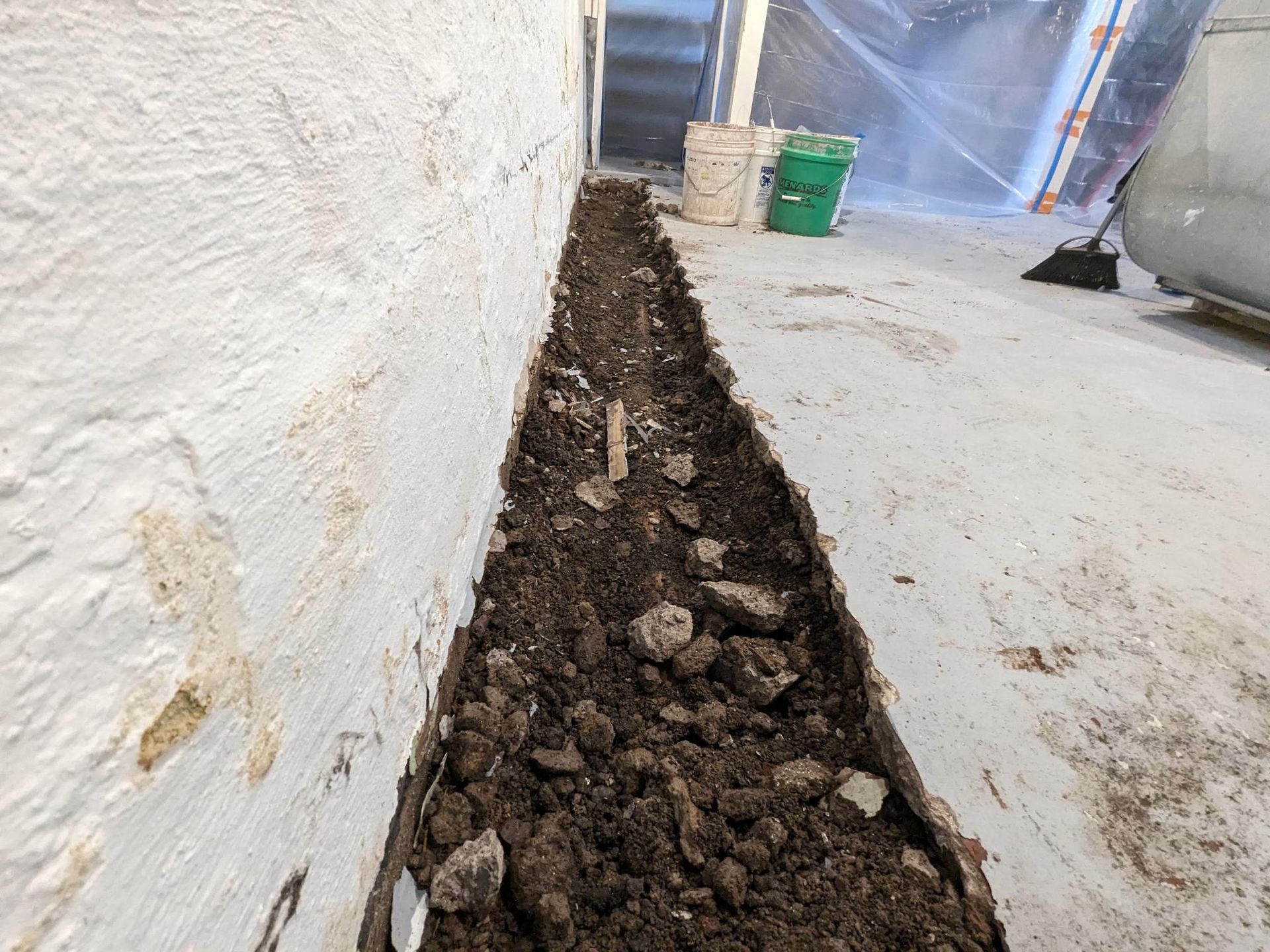 A person is digging a hole in the ground next to a wall.