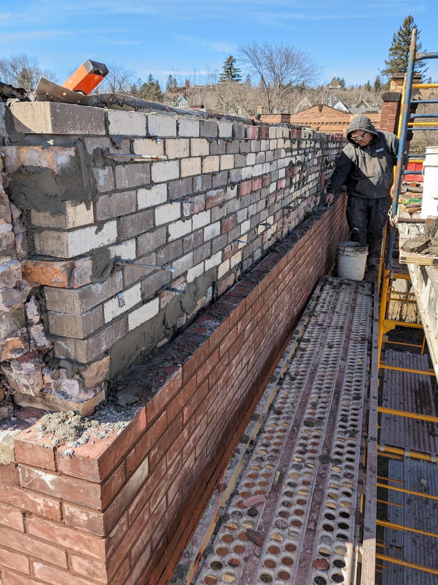 A man is working on a brick wall on a scaffolding.