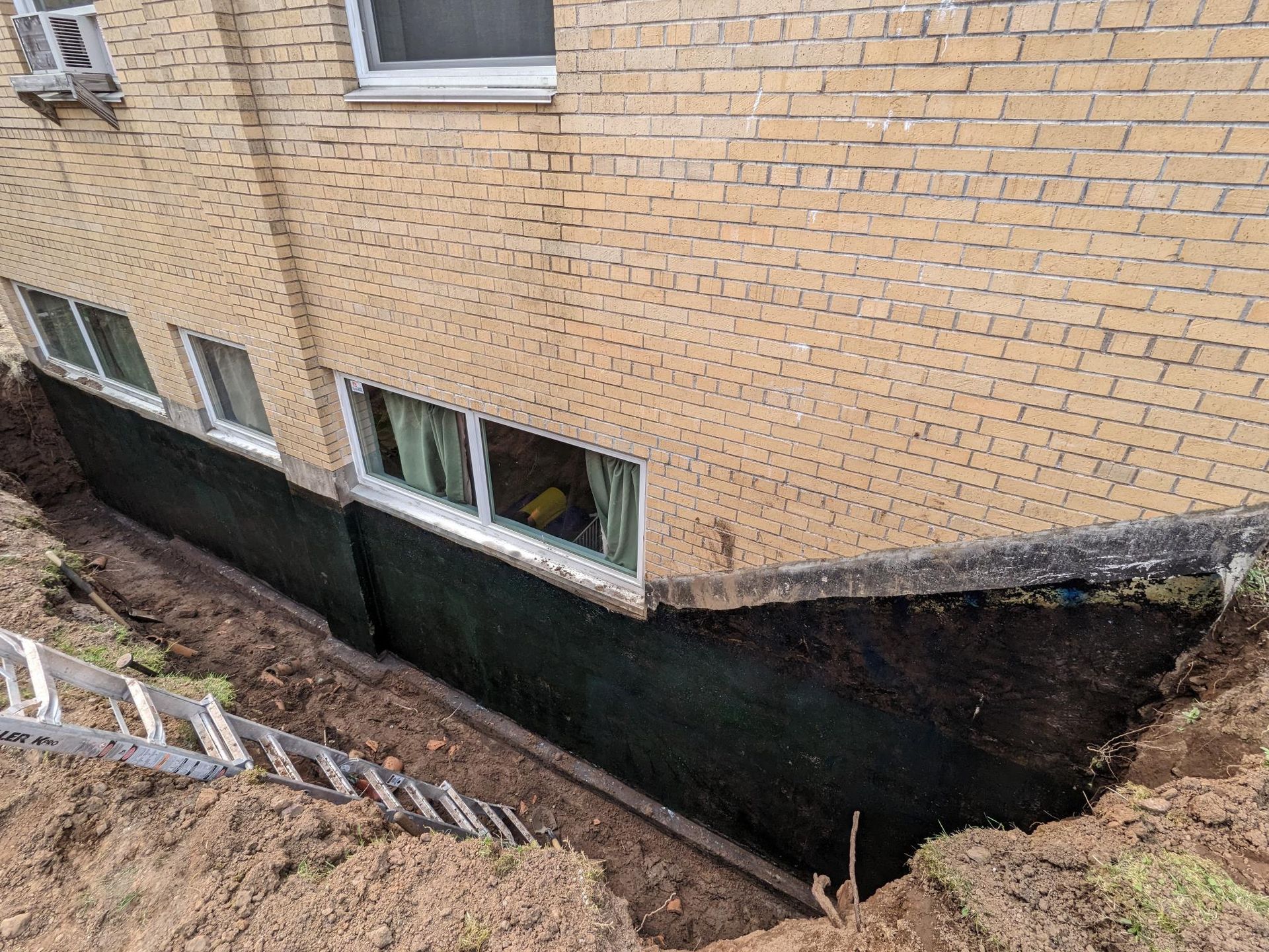 A ladder is sitting on top of a pile of dirt next to a brick building.