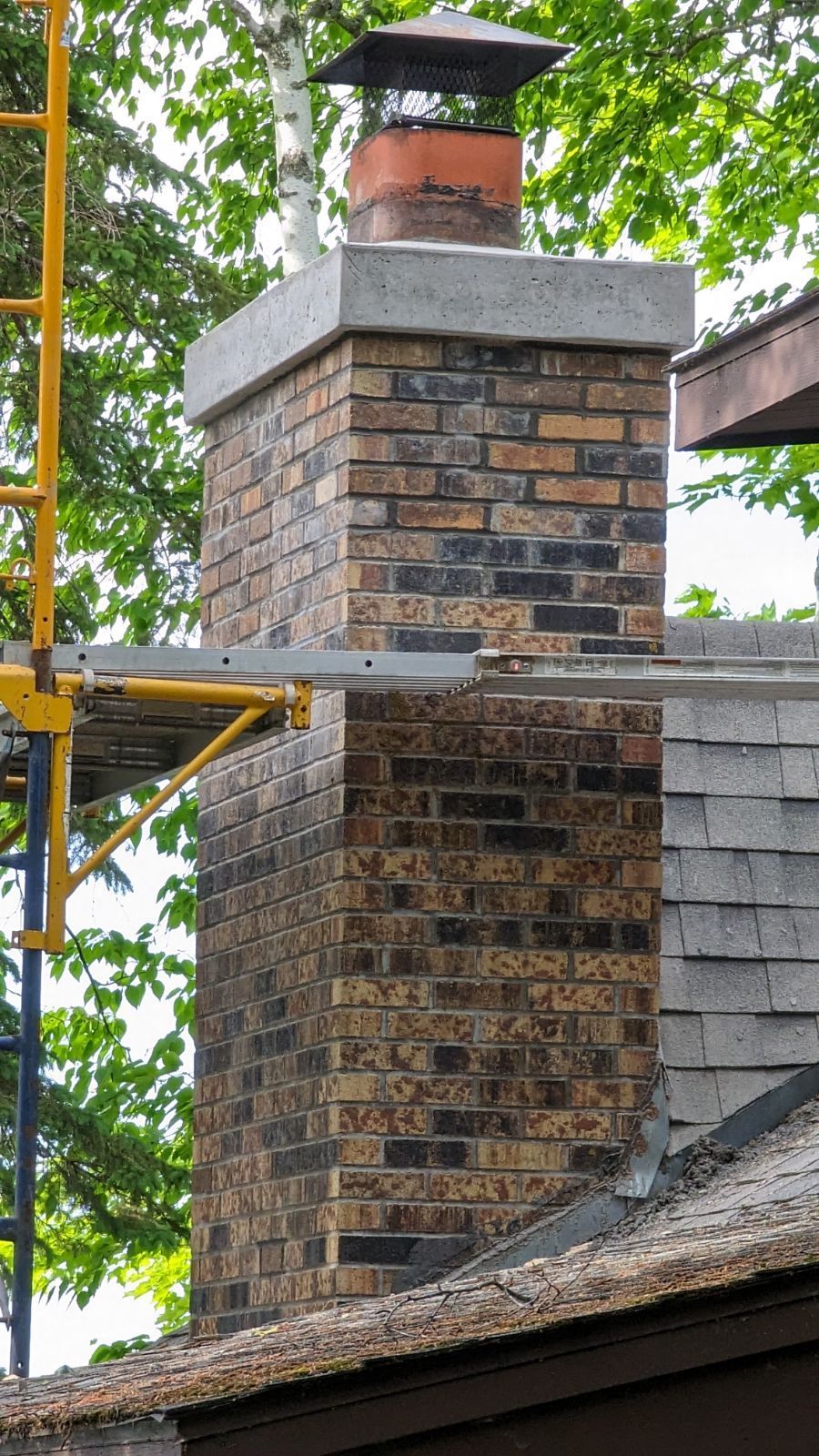 A brick chimney is sitting on top of a roof next to a scaffolding.