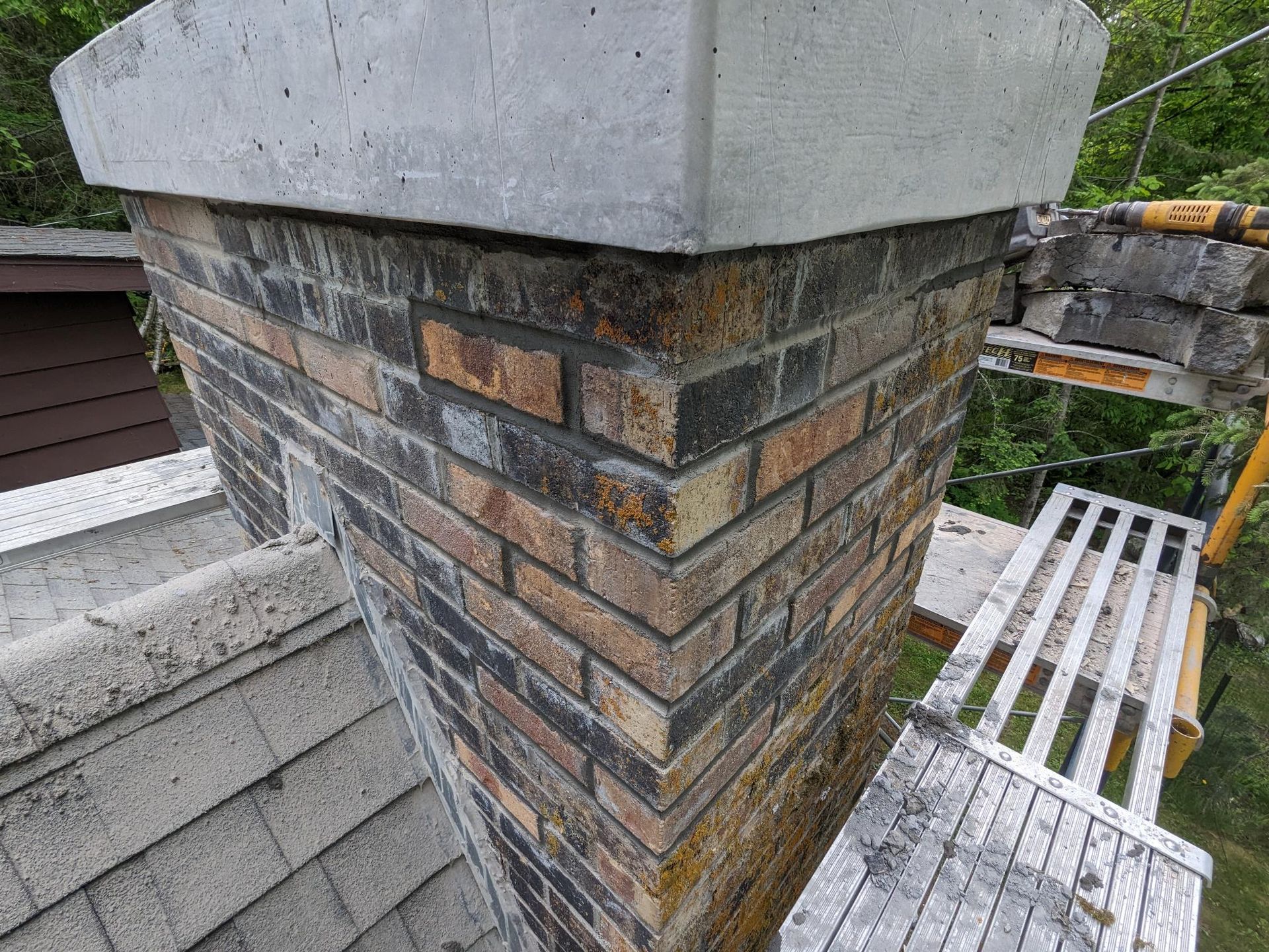 A brick chimney is sitting on top of a roof next to a scaffolding.