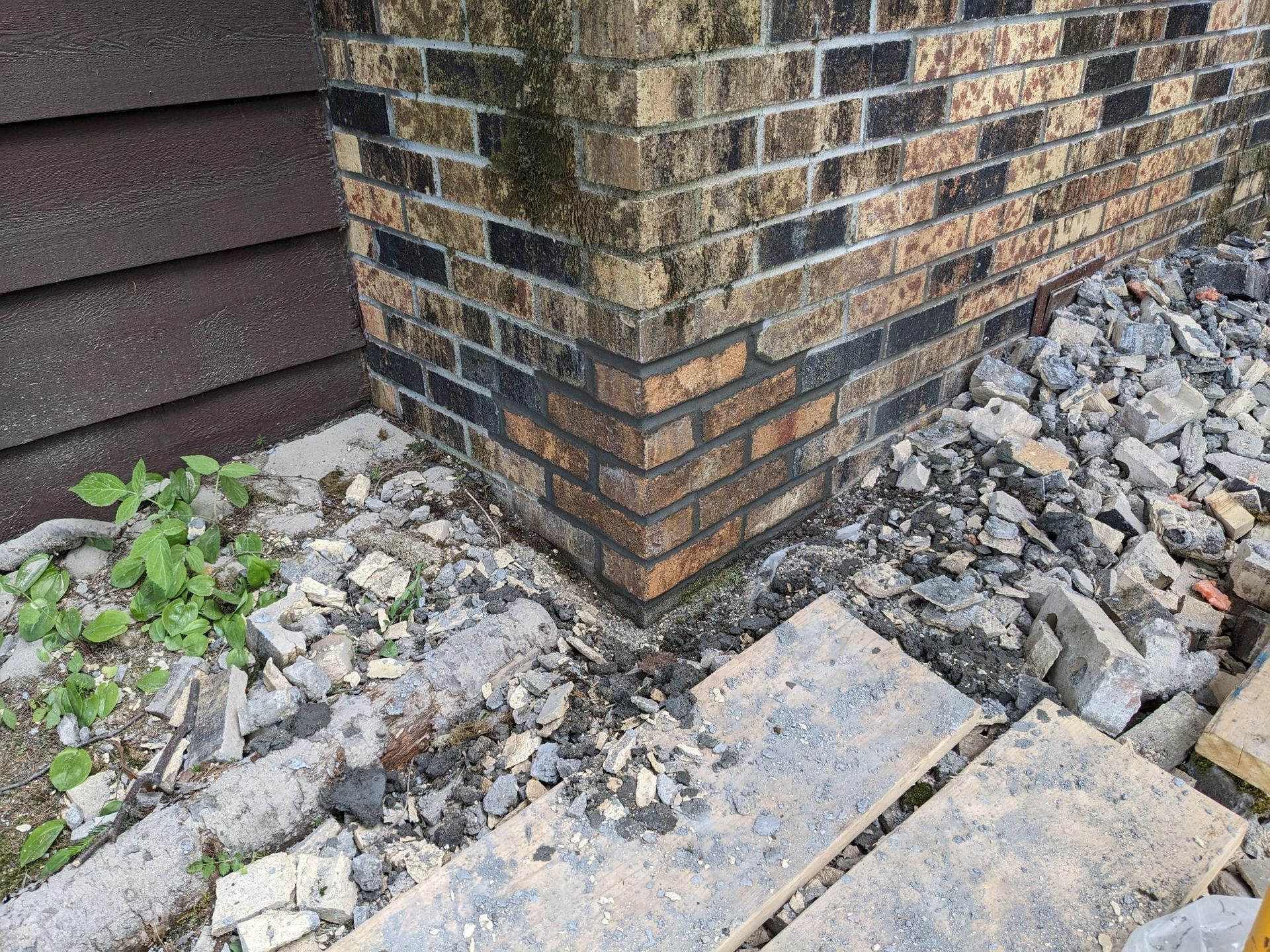 A brick wall with a lot of rocks on the ground in front of it.