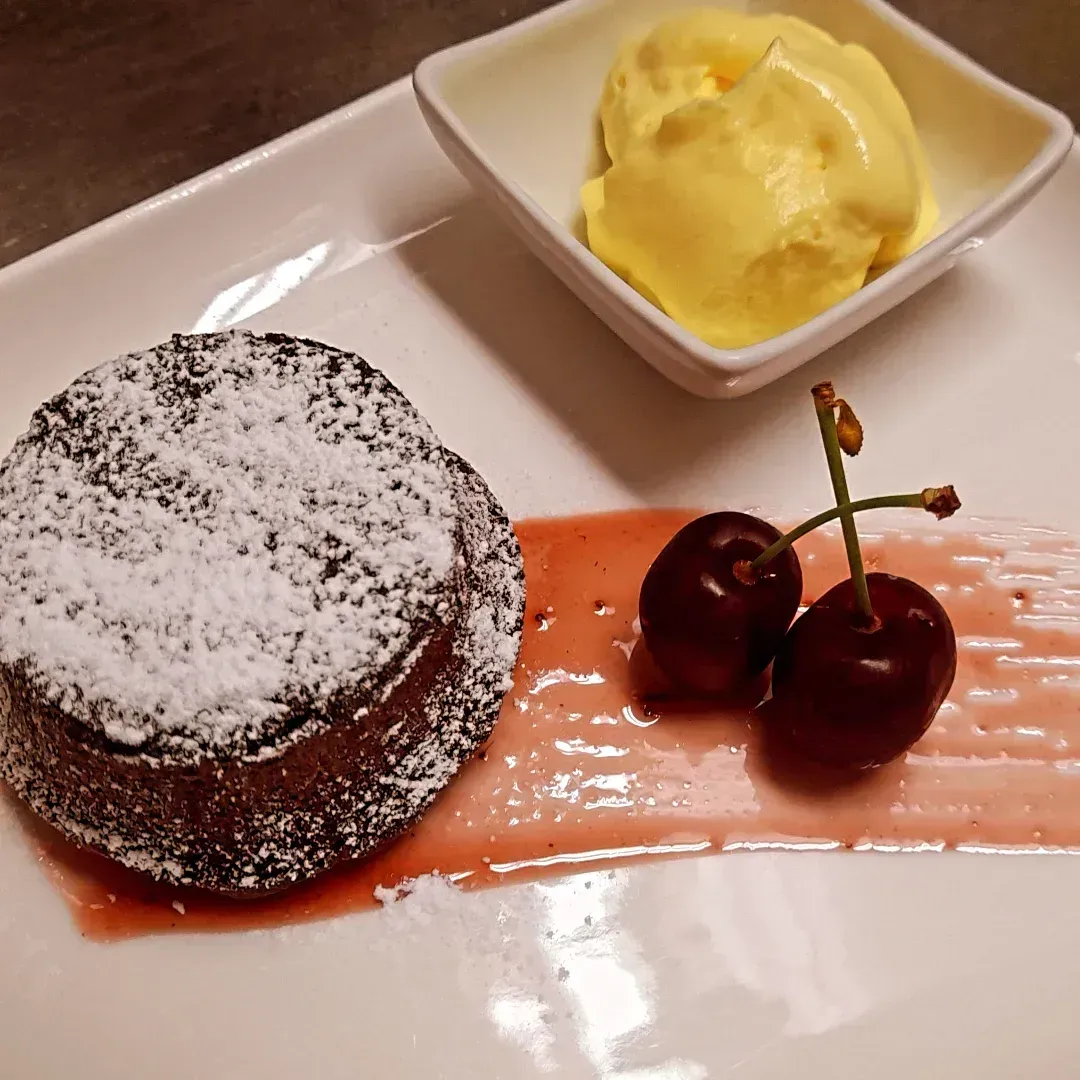 Torta al cioccolato fuso con zucchero a velo, gelato alla vaniglia e ciliegie su un piatto bianco.
