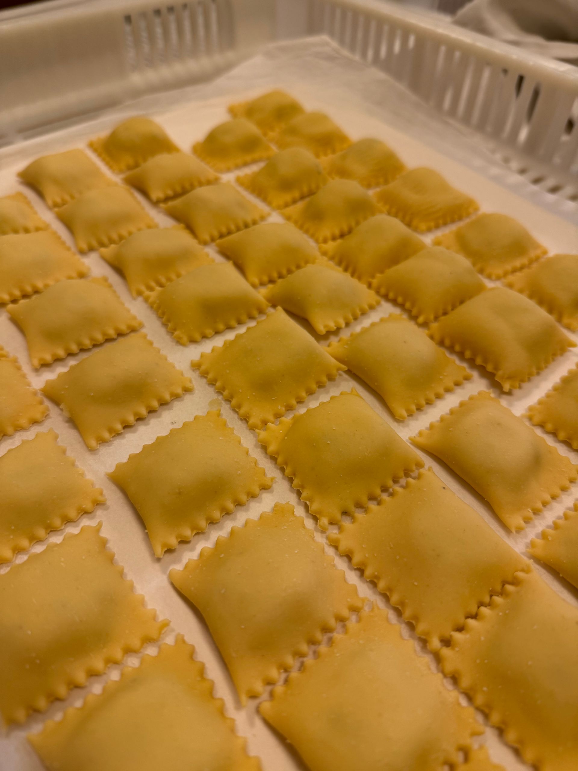 Vassoio di ravioli quadrati appena fatti, con i bordi arricciati, disposti in file ordinate.