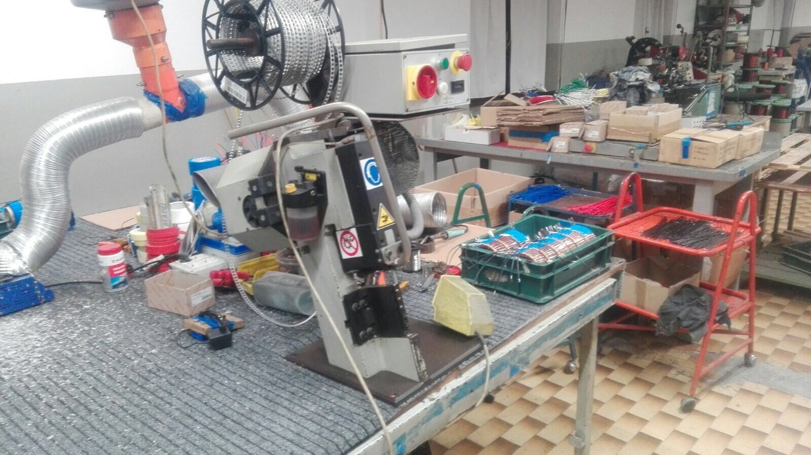 Braccio robotico sopra un banco da lavoro in un laboratorio, con strumenti, cavi e componenti elettronici sparsi sul tavolo.