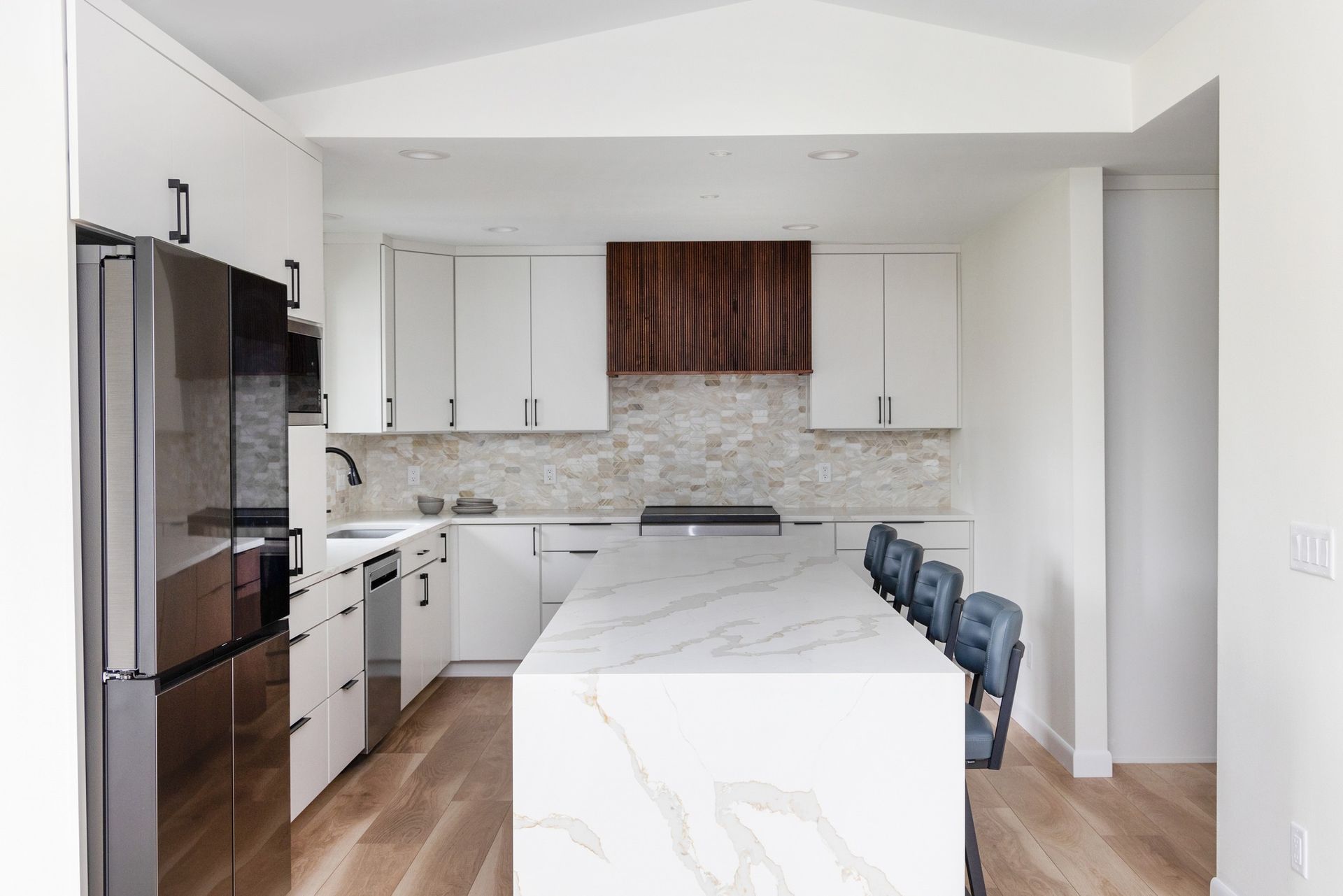 Modern kitchen with white cabinets, island, wooden range hood, and stainless steel appliances.