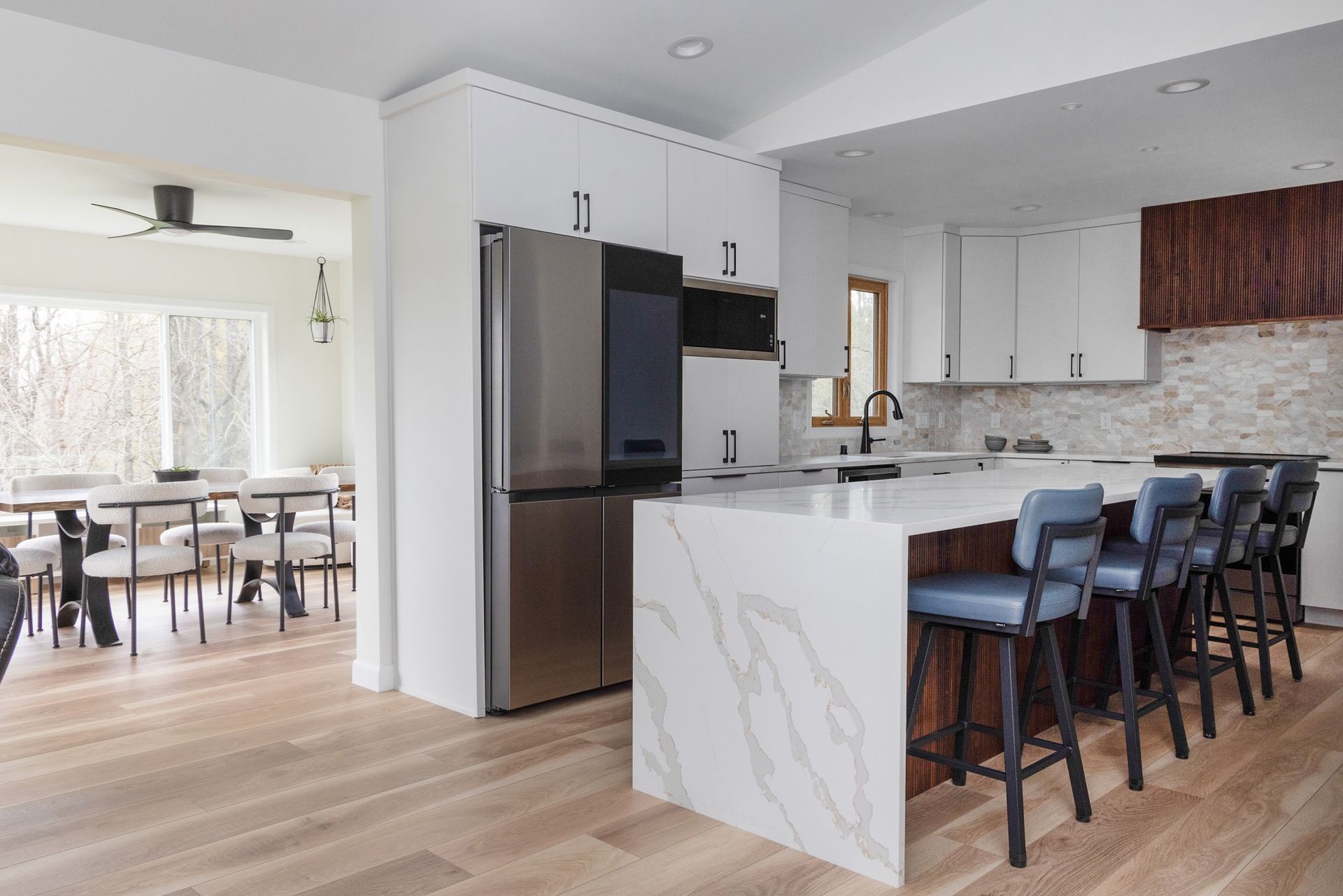 Modern kitchen with island, stainless steel fridge, white cabinets, and dining area in the background.