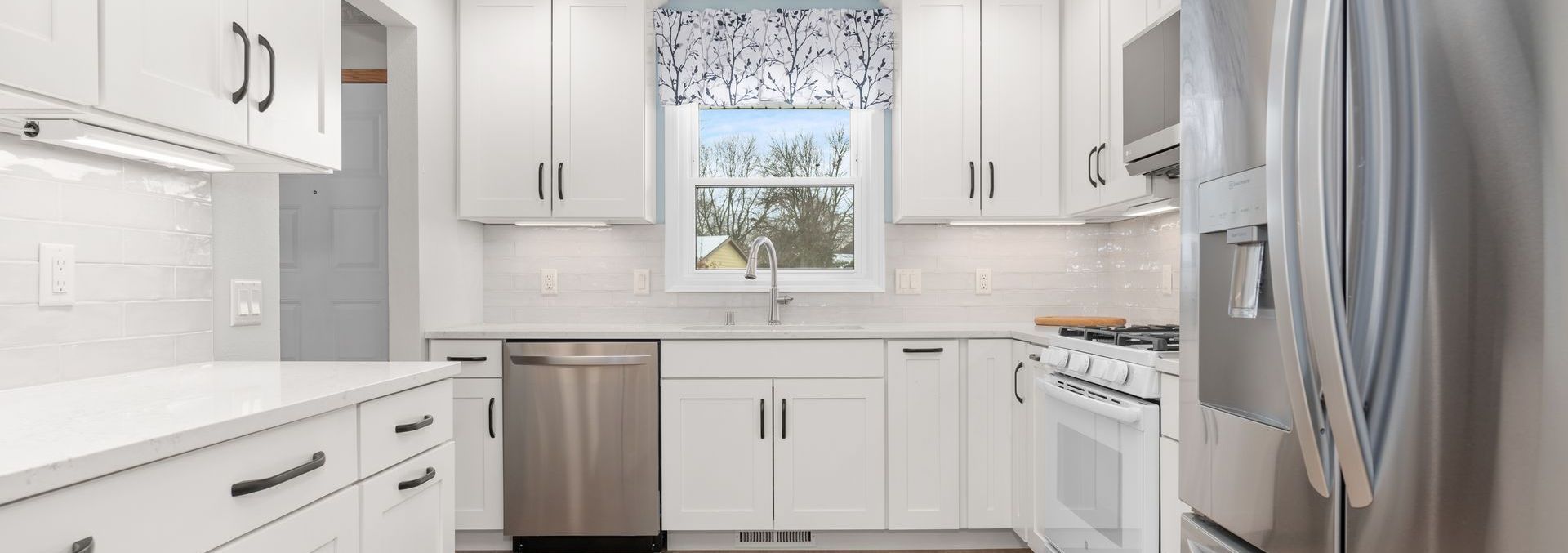 A kitchen with white cabinets , stainless steel appliances , and a window.