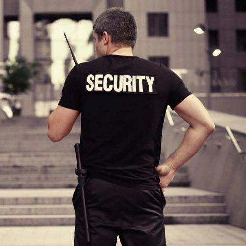 Security guard in black shirt standing outdoors, seen from behind with 