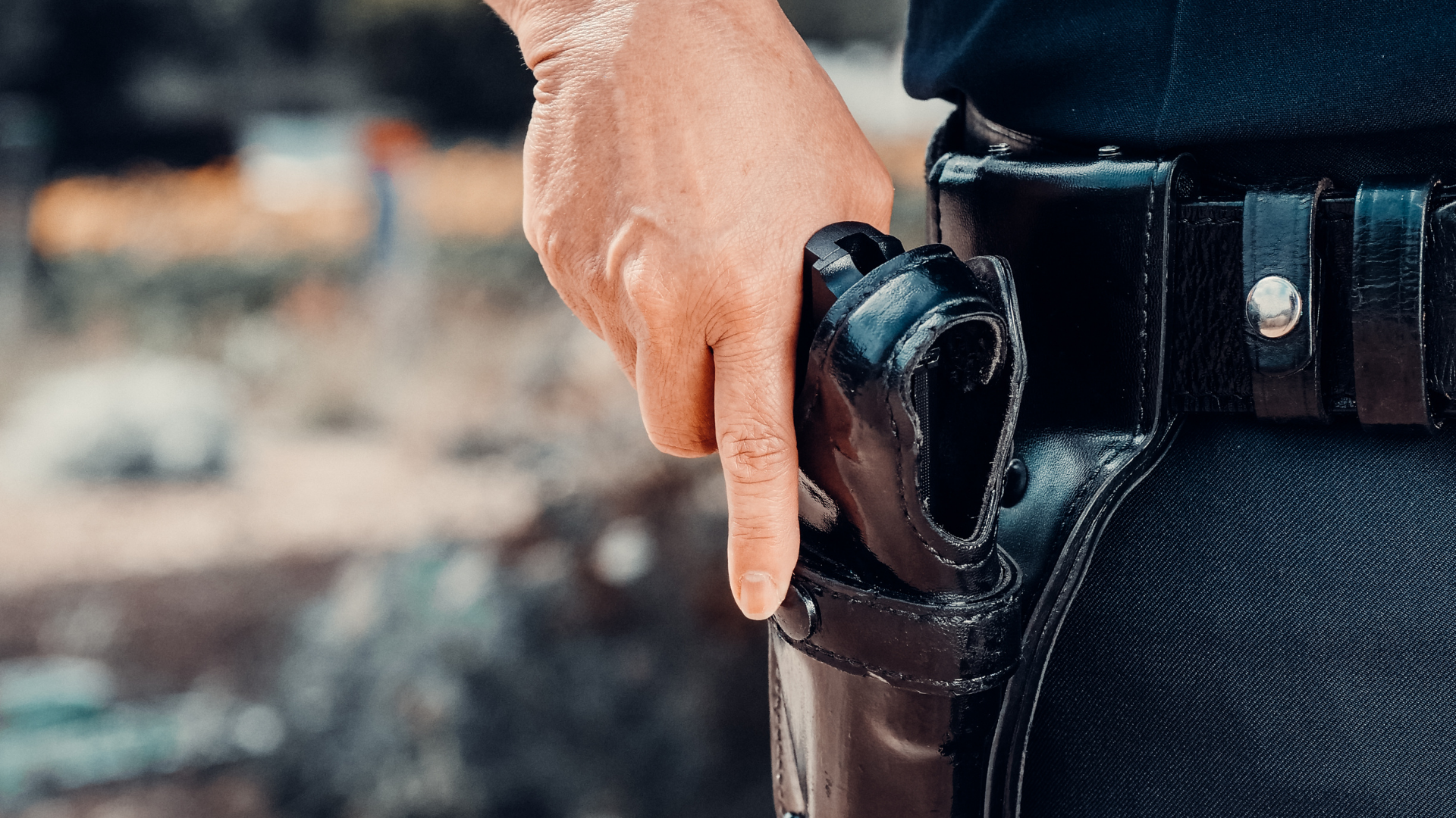 Hand gripping a black handgun in a holster on a person’s belt, close-up
