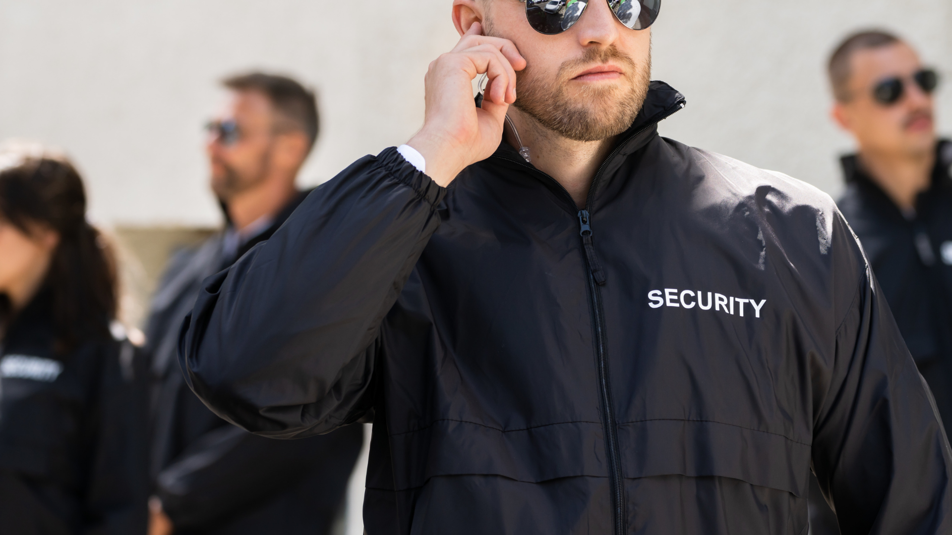 Security guard in black jacket and sunglasses talking on a phone outdoors