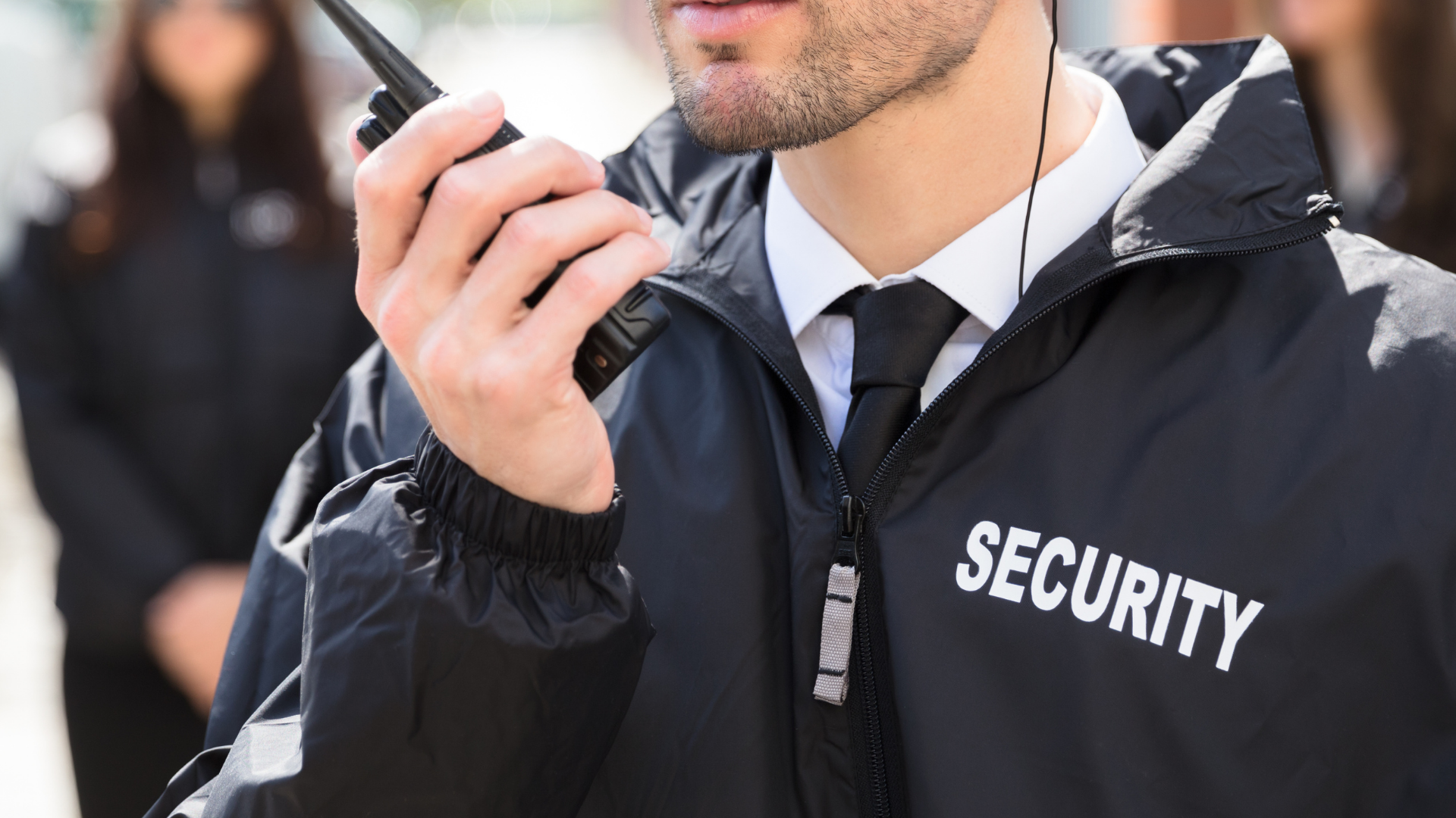 Security guard in black jacket using a handheld radio outdoors
