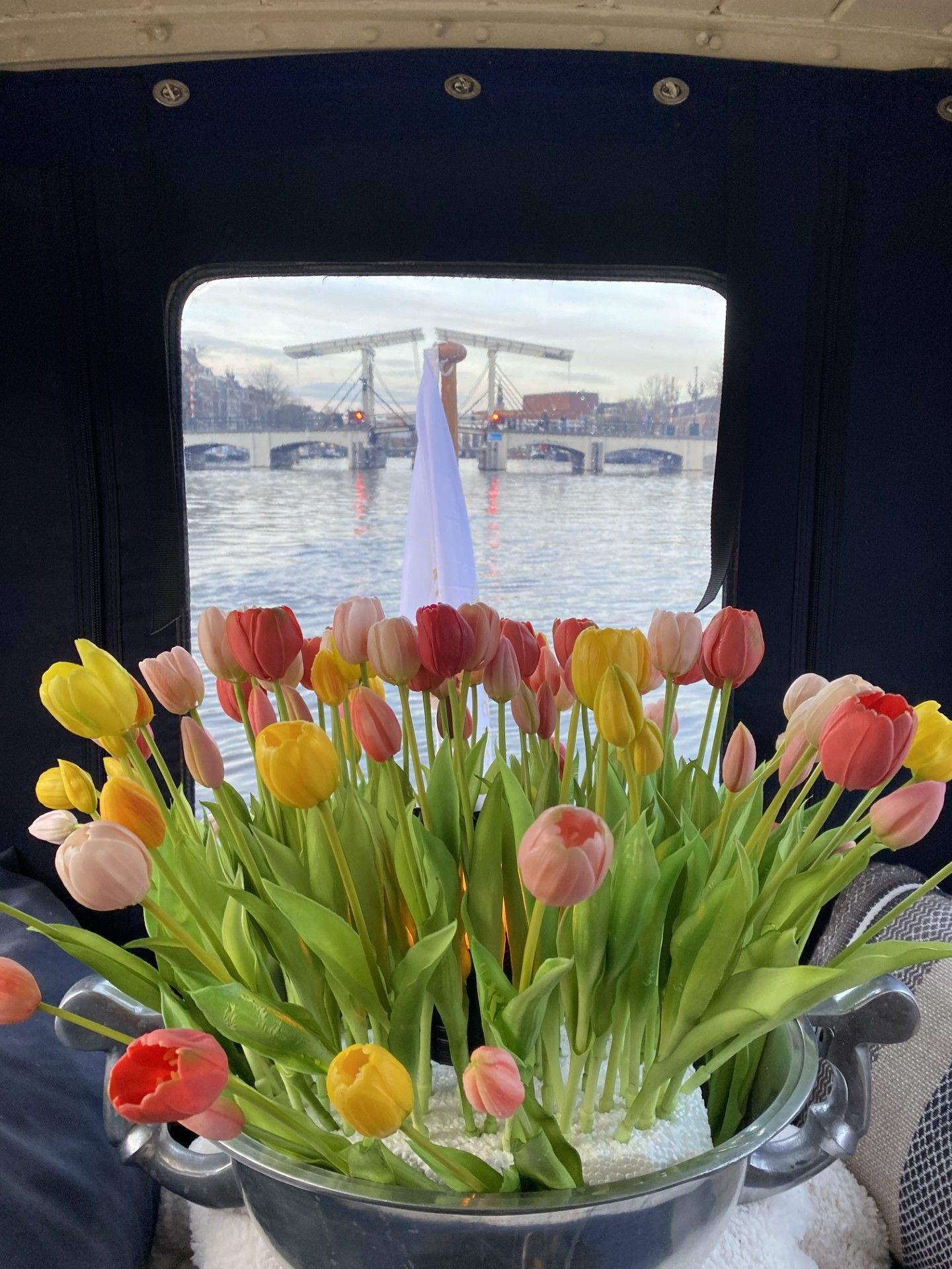 Boat cruising Amsterdam canal, table set with wine and snacks; Westerkerk tower in the distance.