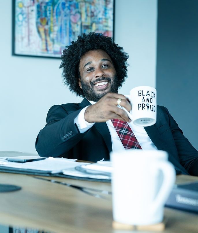 Man smiling at a desk, holding a white mug in a bright office