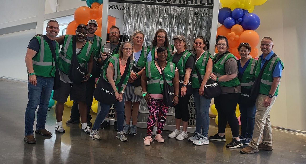 A group of people in green vests are posing for a picture in front of balloons.