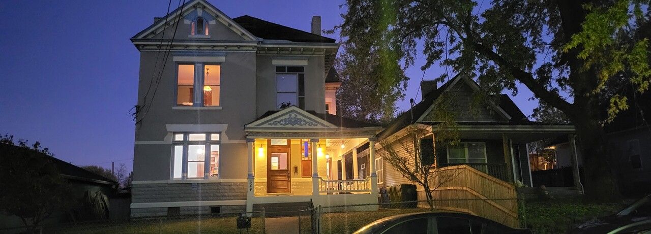 A large house is lit up at night with a car parked in front of it.