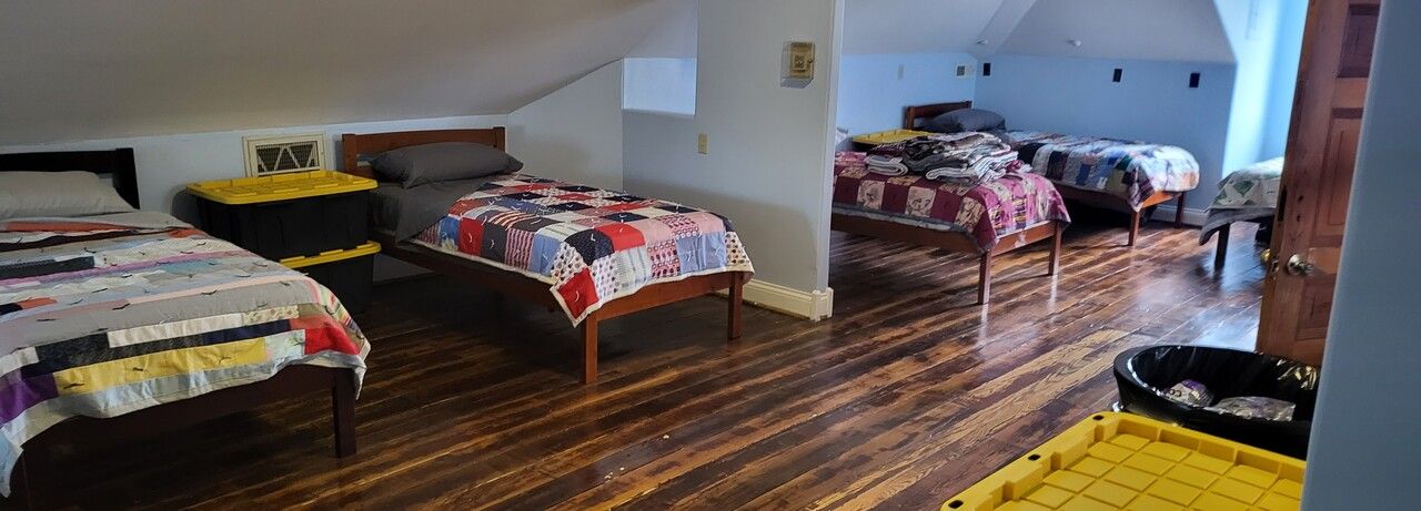 A bedroom with three beds and a trash can on the floor.