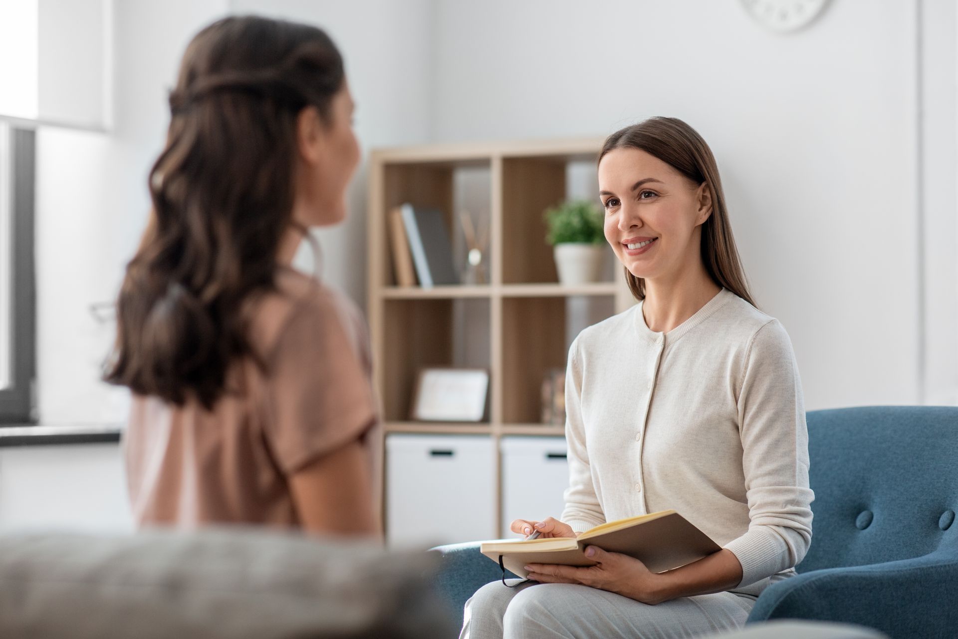 A woman is sitting in a chair talking to a young girl.