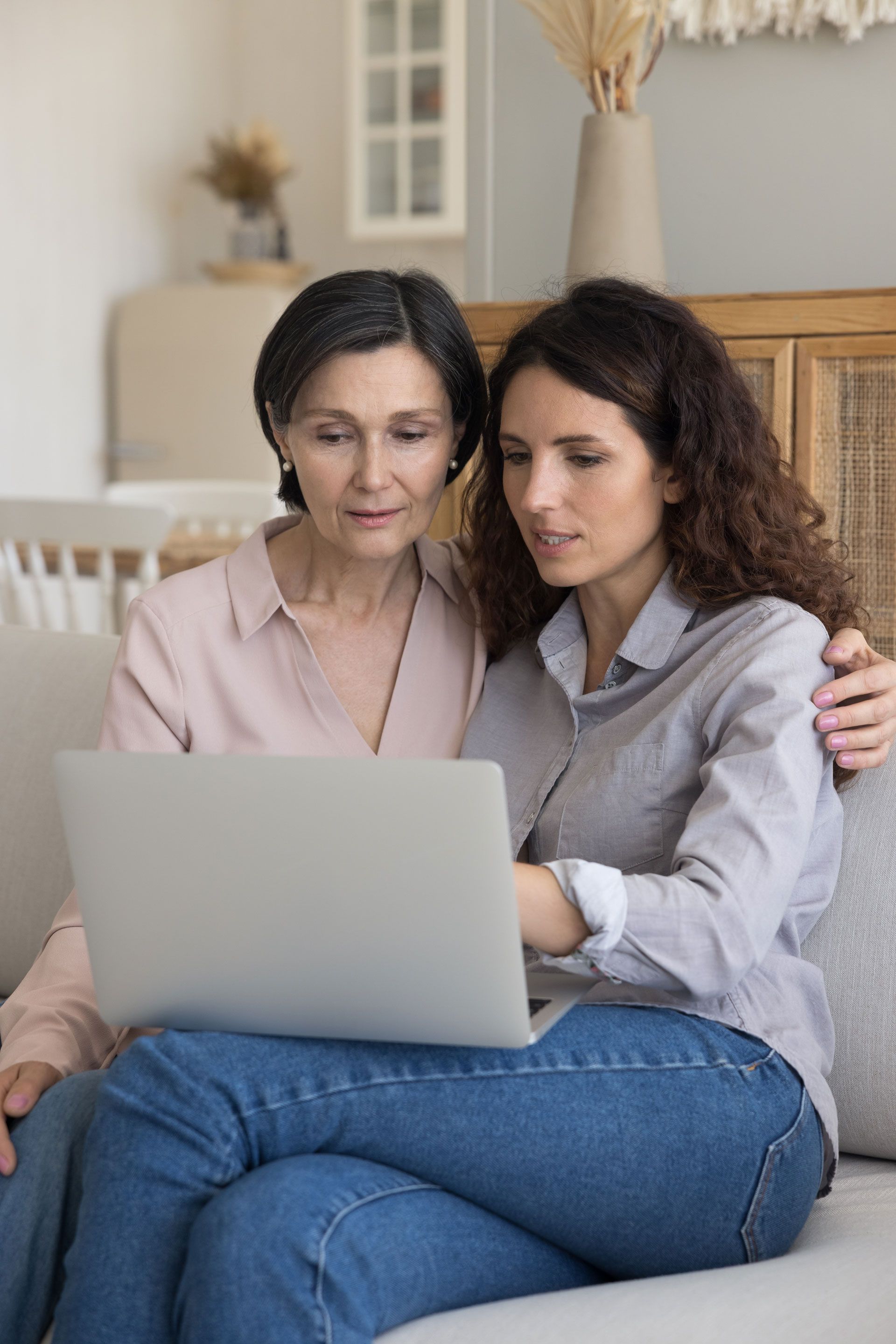 Two women are sitting on a couch looking at a laptop computer.