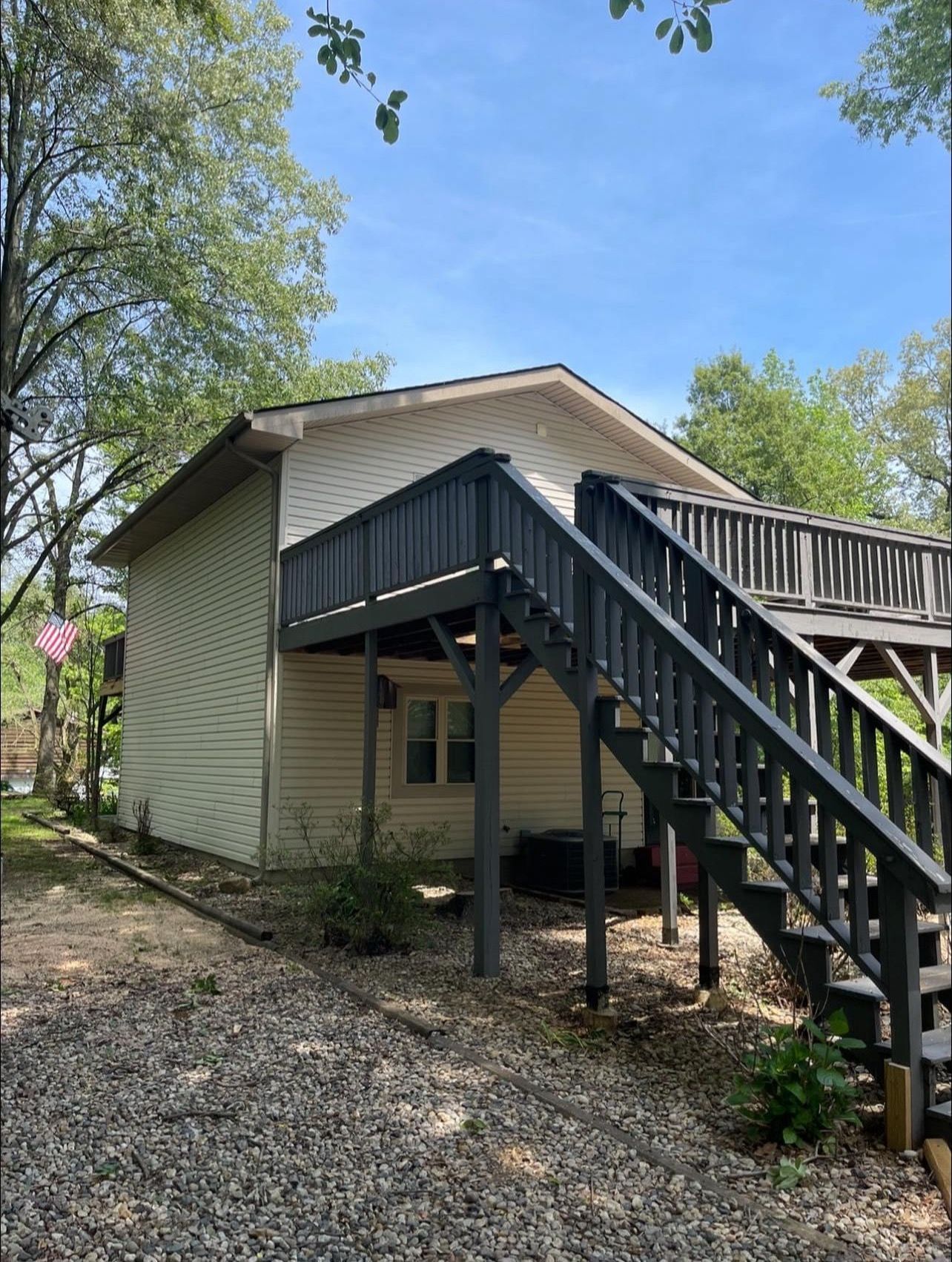 A white house with a black deck and stairs leading up to it.