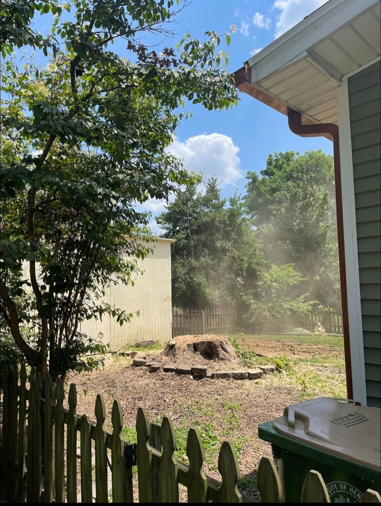 A house with a fence and a trash can in front of it