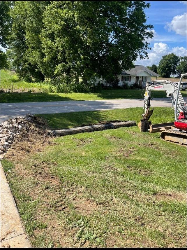 A red excavator is digging a hole in the grass in front of a house.