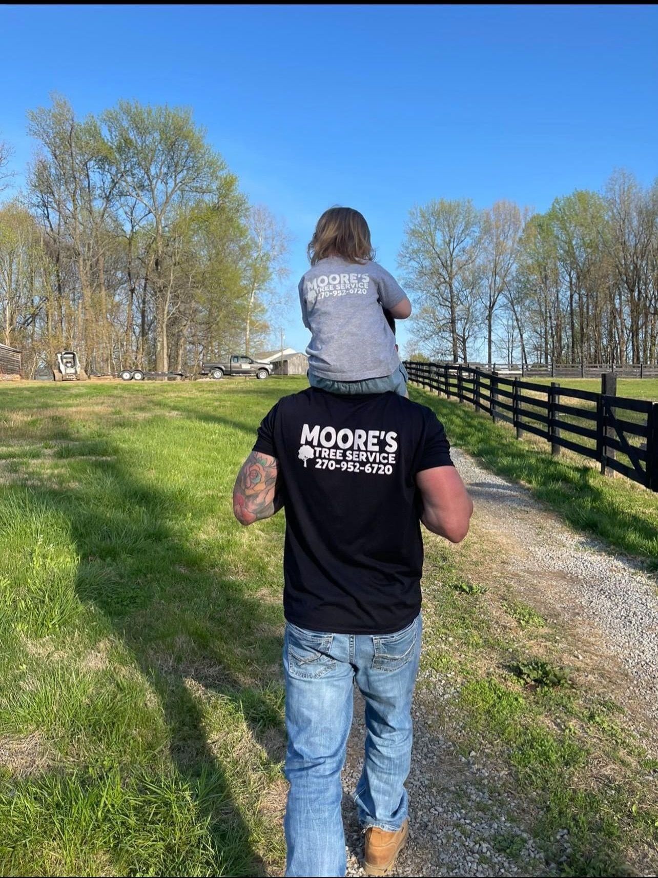 A man is carrying a child on his shoulders down a dirt road.