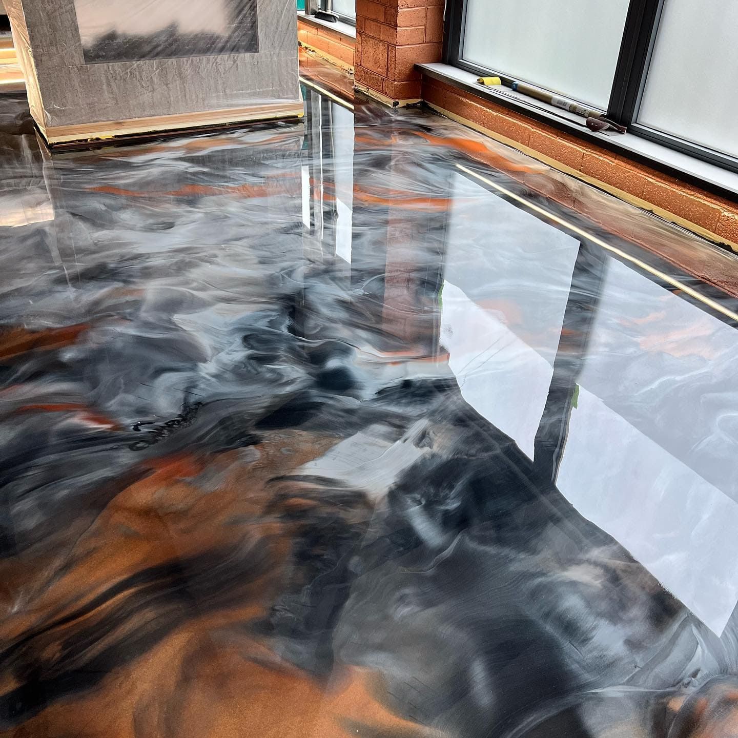 Glossy epoxy floor with swirling black, copper, and white color. Reflecting window light.