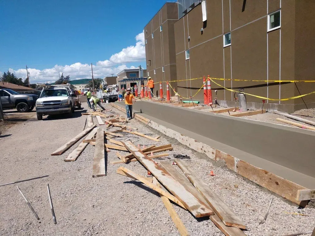 A group of construction workers are working on a sidewalk in front of a building under construction.