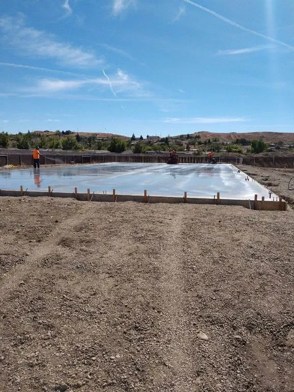 A large concrete slab is being poured in a dirt field.