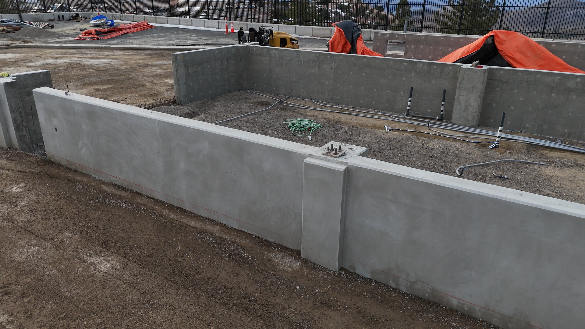 Two red fire extinguishers are on the ground in front of a concrete wall