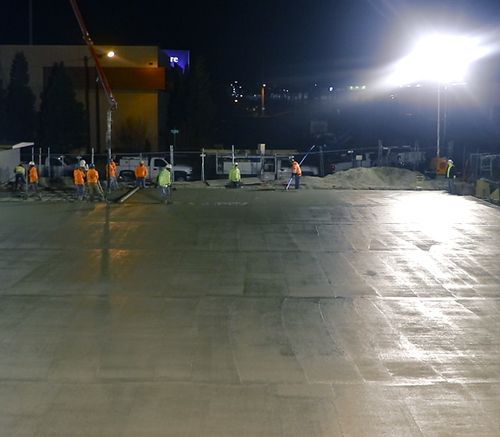 A group of construction workers are working on a concrete floor at night.