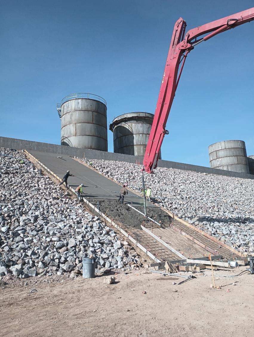 A red crane is being used to pour concrete on a rocky hillside.