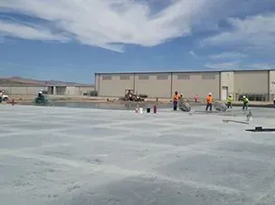 A group of construction workers are working on a concrete floor in front of a building.