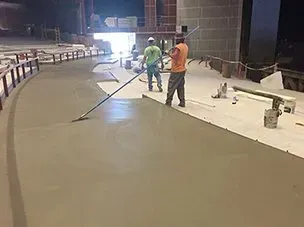 Two men are working on a concrete floor with a broom.