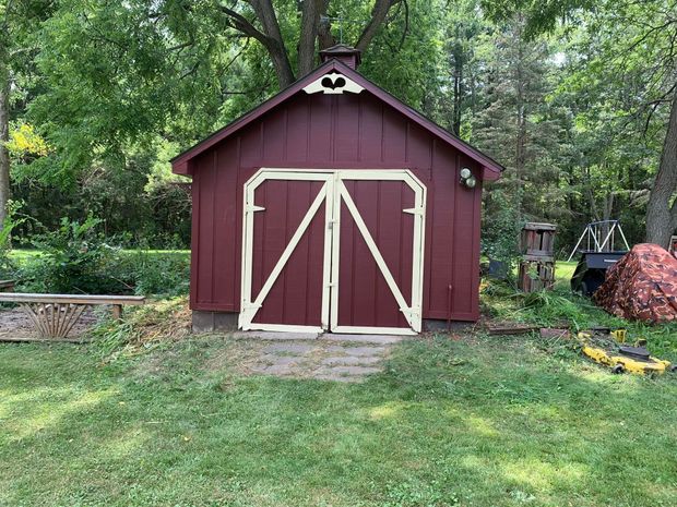 Red shed with white-trimmed double doors in a grassy yard, surrounded by trees.