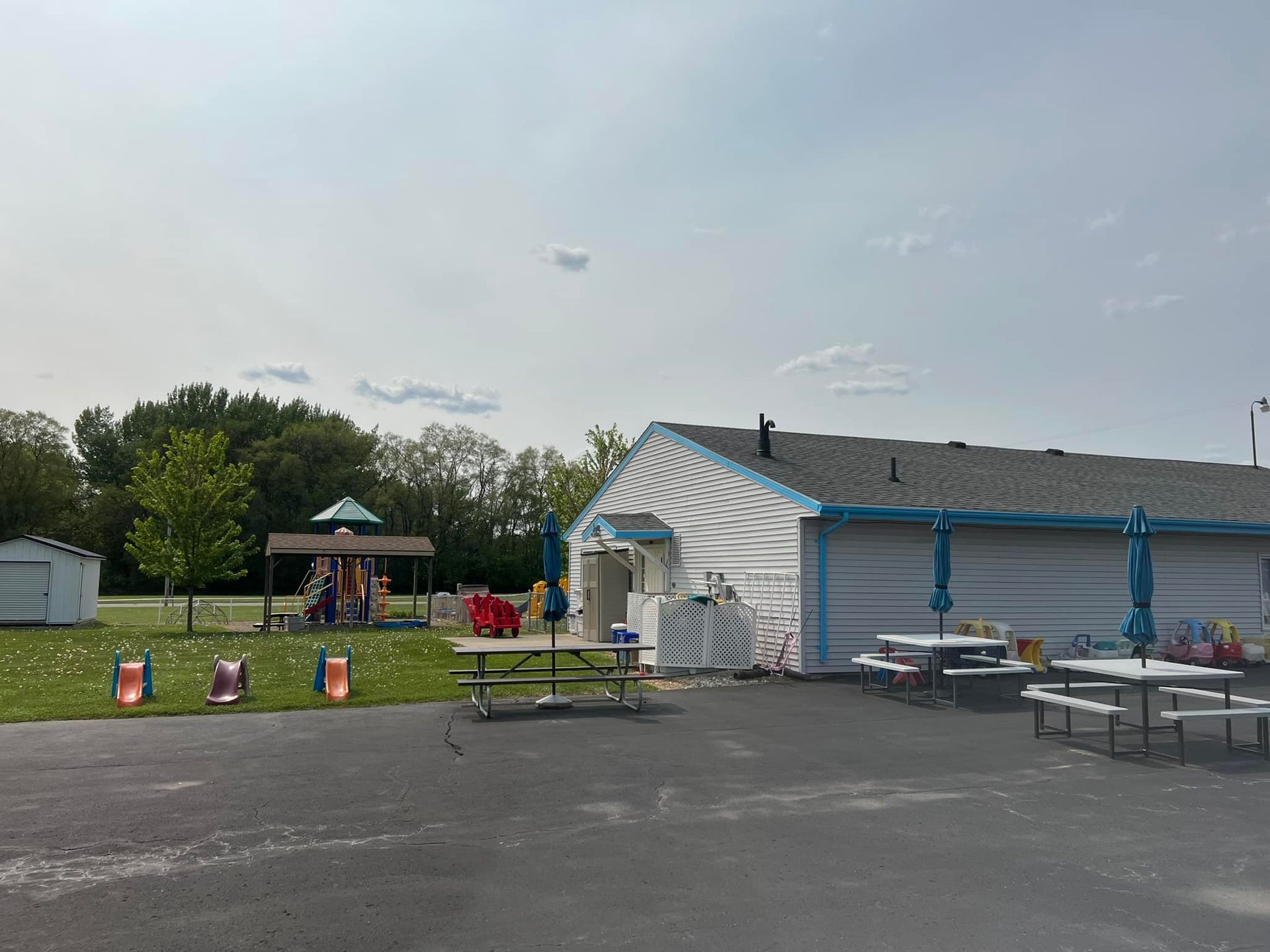 An ice cream shop with outdoor seating, a playground, and a lawn under a cloudy sky.