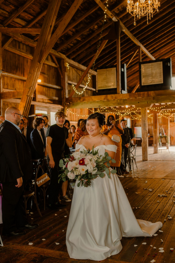 A bride is walking down the aisle at her wedding at the Gallagher Wedding Barn