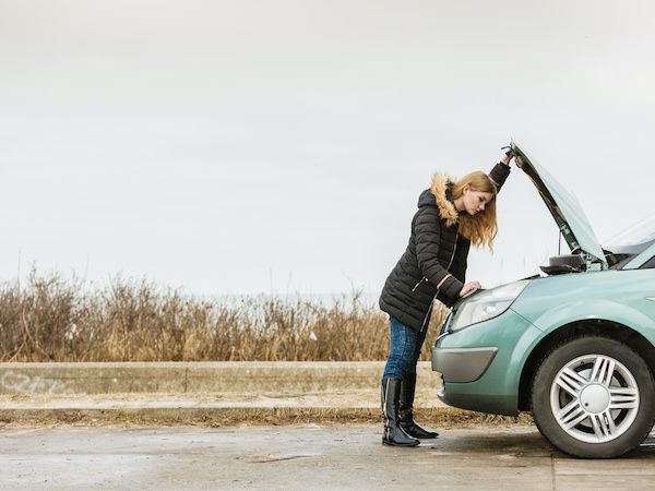Woman with a broken-down teal car, examining the engine in a field. | Torque European Car Care