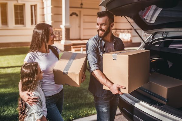 Family loading cardboard boxes into a car trunk outside their new home; sunny day. | Torque European Car Care