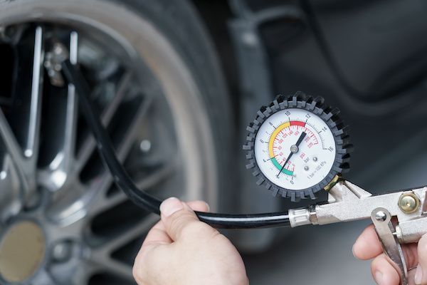 Person checks car tire pressure with a gauge. | Torque European Car Care